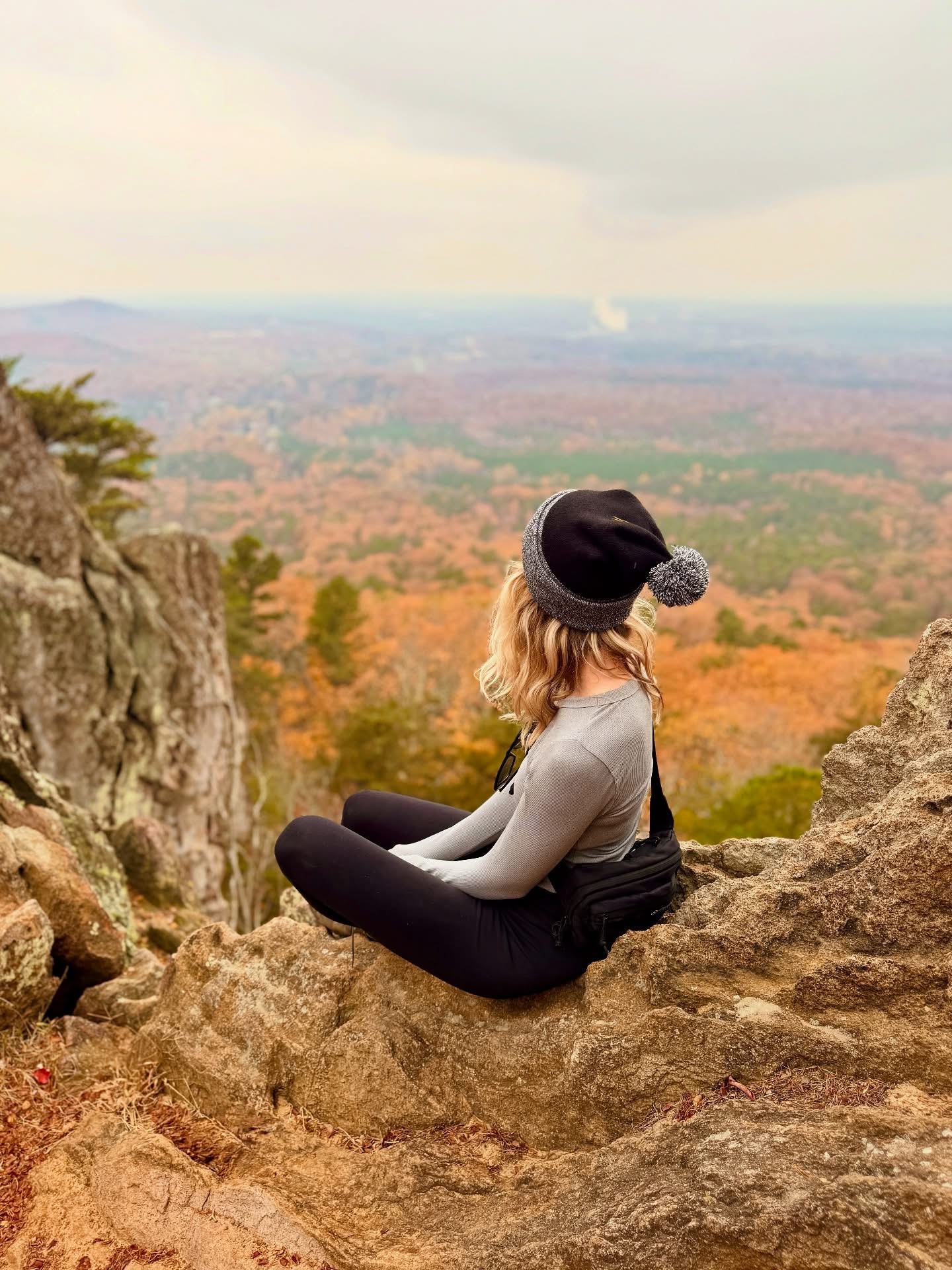 Nicole sitting on a rocky overlook with autumn foliage
