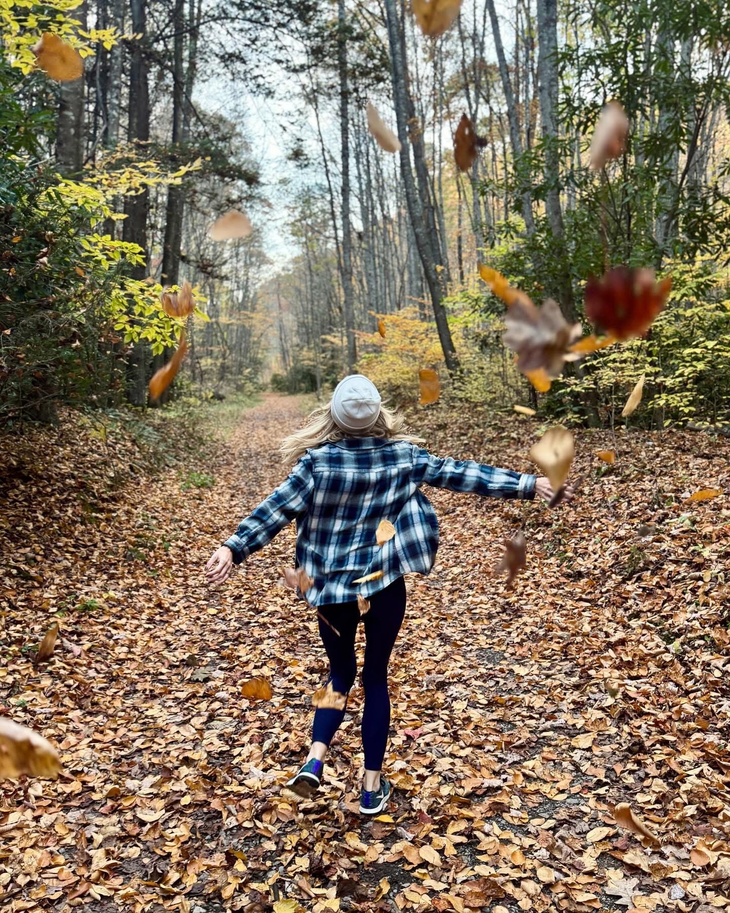 Nicole running down a leaf-strewn forest road throwing autumn leaves