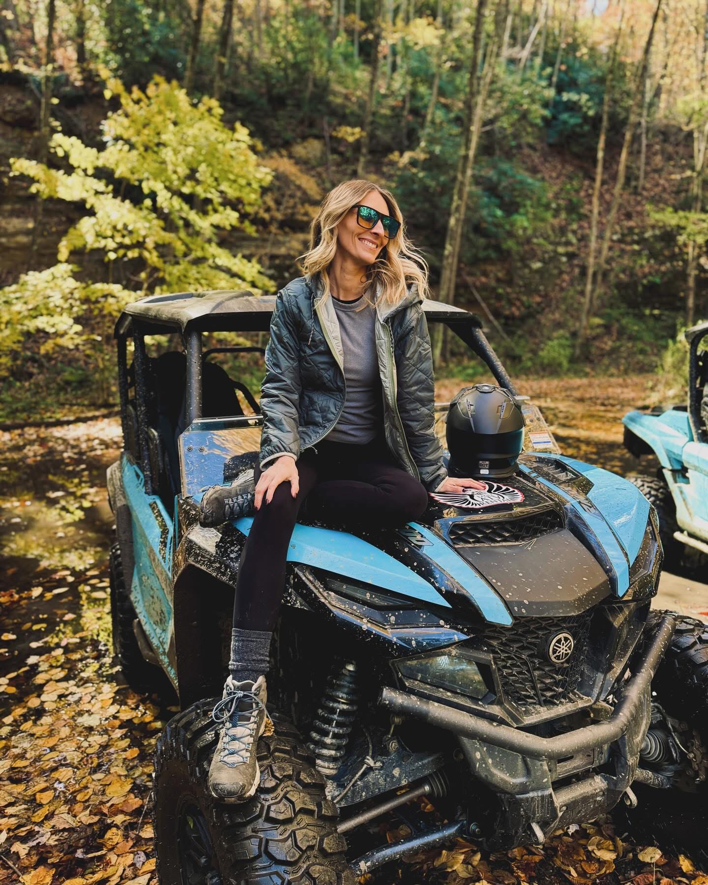 Nicole sitting on the hood of a blue Yamaha RMAX in the woods